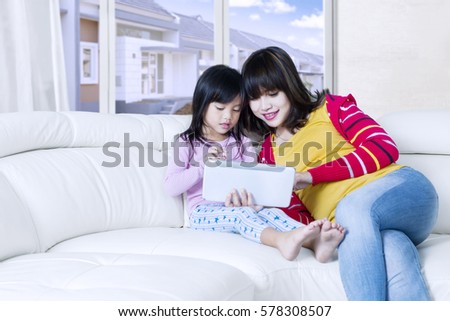 Young Asian woman and her daughter sitting on the sofa while using a digital tablet at home