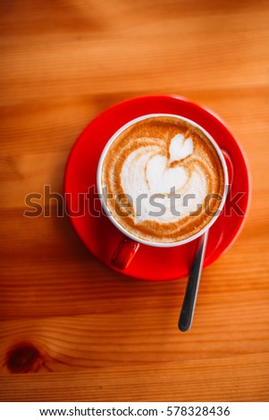 Hot latte with latte art on wood table in red mug with selective focus on the latte art.vintage colour