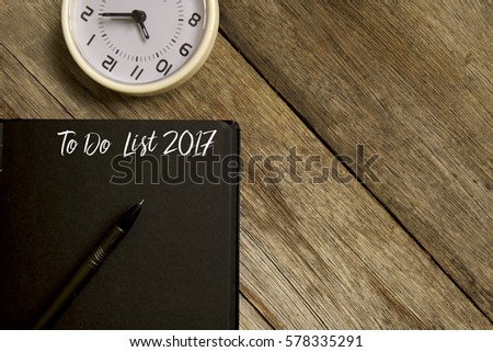 Business concept. Top view of  table clock, pen and notebook written with TO DO LIST 2017 on wooden background. Copy space. Flat lay.