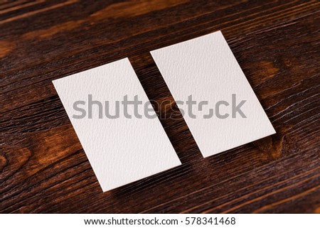 Closeup mockup of two blank vertical business cards at brown wooden table background.
