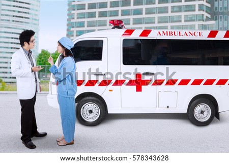 Picture of mae doctor and his partner discussing together while standing near the ambulance car 