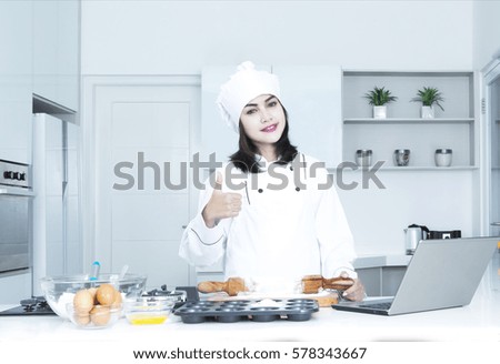 Portrait of a pretty female baker smiling at the camera while showing thumb up in the kitchen