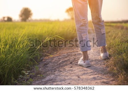 Picture of feet of woman (lonely girl),wearing white sneakers and blue jeans.Foot of female (traveler) Walk toward successful on path way and green fields beside.Travel and success concept
