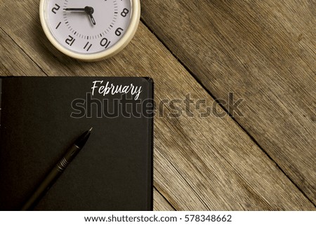 Business concept. Top view of  table clock, pen and notebook written with FEBRUARY on wooden background. Copy space. Flat lay.