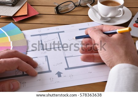 Designer working on an interior design project on wood table with a house plan, tools and samples. Elevated view