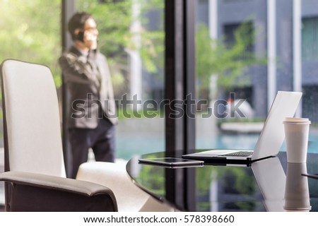 Closeup technology laptop and tablet with paper coffee cup on the working space in modern office over the photo blurred of Happy asian businessman standing background. business communication concept.