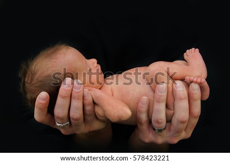 Tiny Newborn Premature Baby being held in father's hands Royalty-Free Stock Photo #578423221