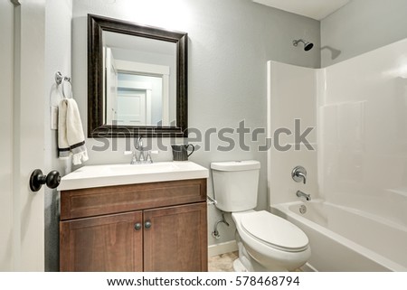 Compact light bathroom with soft gray walls highlighting a brown sink vanity accented with wood framed vanity mirror. Northwest, USA