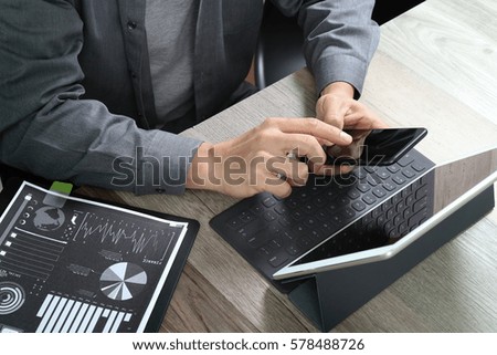 top view of businessman using smart phone for mobile payments online shopping with digital tablet docking keyboard computer and documents on wooden desk in modern office 