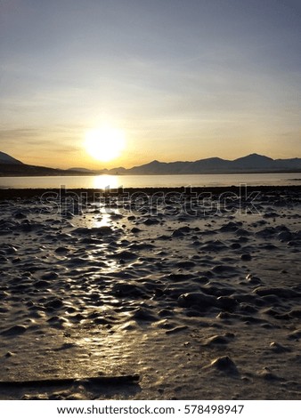 bright yellow sunrise over cold fjord and mountains with reflection on thick frozen sea shore ice