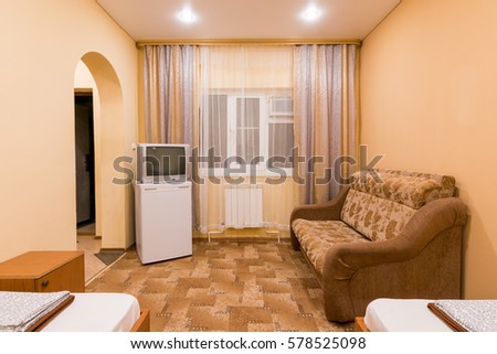 The interior of a small room with sofa bed and two single beds, window, TV and fridge Royalty-Free Stock Photo #578525098