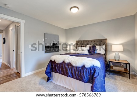 Lovely master bedroom with soft grey walls, queen bed with tufted headboard and dressed in dark blue bedding and white faux fur throw blanket, and boasts reclaimed wood nightstands topped with lamps. 