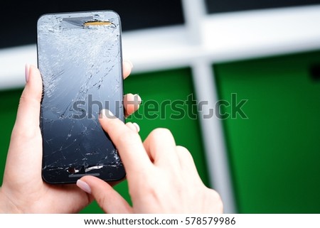Young woman trying to use a broken glass mobile phone on colored background