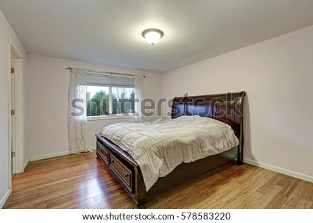 White bedroom with dark stained wood bed with lower drawers atop bamboo wood floors. Northwest, USA