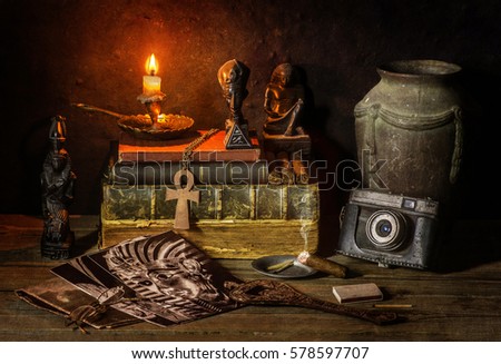 Classic still life with vintage books placed with old jar, illuminated candle, camera,old pictures,cigar and some ancient Egyptian sculptures on rustic wooden background.