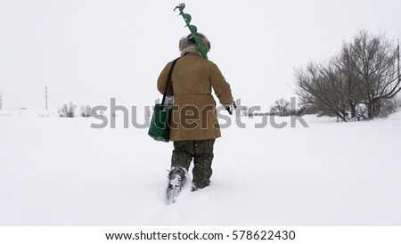 A fisherman walks on a snow-covered lake in search of a good fishing place