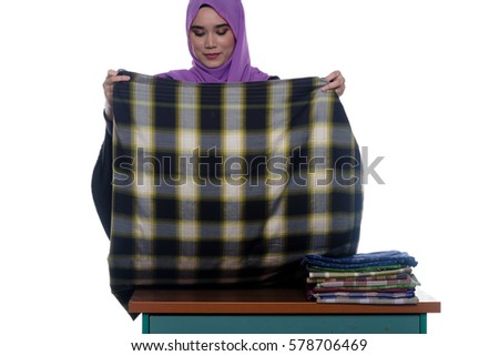 A pretty young muslim lady is busy folding clothes isolated on white background