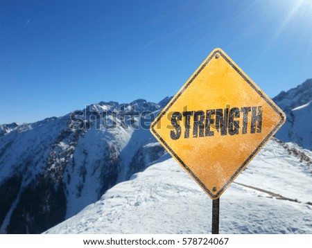Strength, yellow frosted motivational sign with snow, sun, blue sky and mountains in the background