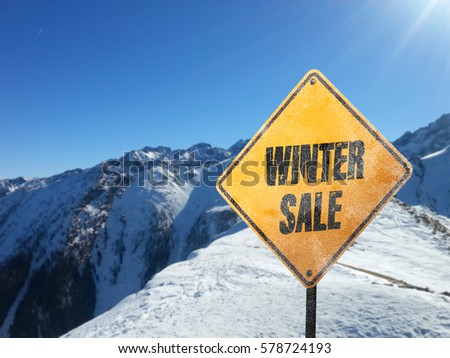 Winter Sale, yellow frosted sign with snow, sun, blue sky and mountains in the background
