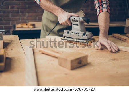 closeup photo of cabinetmaker grinds wooden plank on tabletop at workstation. Royalty-Free Stock Photo #578731729