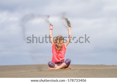 young child girl throwing sand up on empty beach