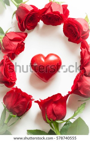 A red heart in the center surrounded by red roses on white board, Valentines Day background, wedding day. Sign of love. Show the appreciation to someone you love. 