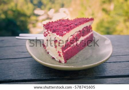 Close-up red velvet cake and white cream on wooden table with nature background in garden.