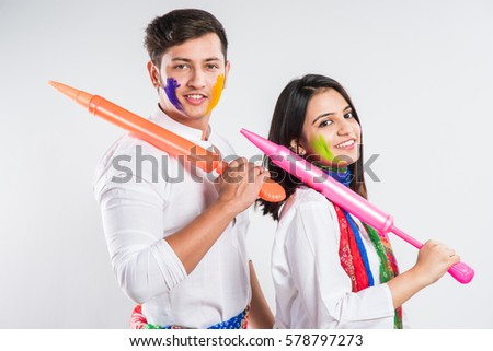 young indian couple holding pichkari on Holi festival, standing isolated over white background with copy space