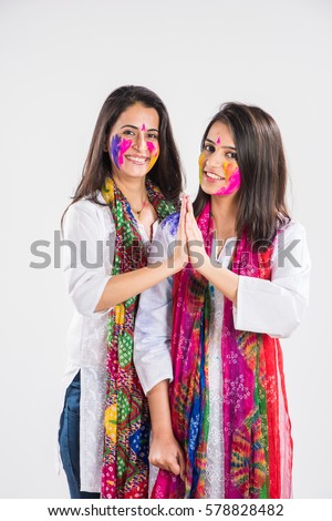 two Indian beautiful girl in namaskar pose or welcoming with hands folded on holi festival, with coloured face, in indian traditional wear and dupatta, isolated over white background with copyspace