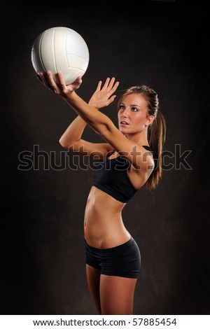 Beautiful young woman playing volleyball over dark background