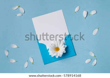 Spring top view composition: blank stationary template / invitation mockup in envelope, scattered petals around, white flower with yellow heart. Sky blue background with copy space for text. Flat lay.