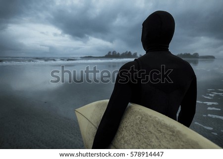 Surfer with a surf board at a sandy beach looking out on Pacific Ocean. Picture taken in Tofino, Vancouver Island, British Columbia (BC), Canada.