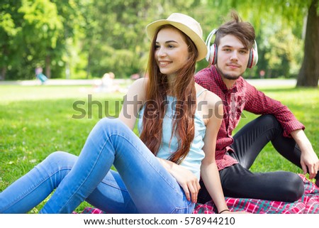 Portrait of a young girl and a guy sitting together on green grass in the park campus.