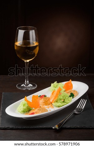 Plate with pumpkin puree and pistachio sponge on a slate cheese board. Fork and a glass of wine, dark background. Gourmet dinner.