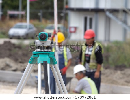Close up of leveling device on road construction site with surveying workers and engineers in background