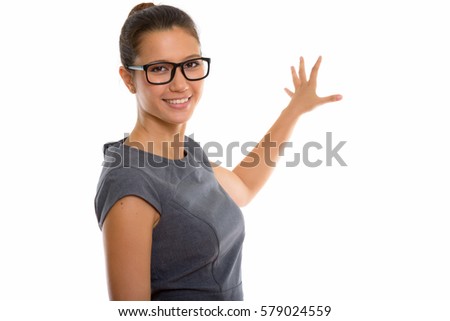 Studio shot of young happy businesswoman smiling while showing something on the wall