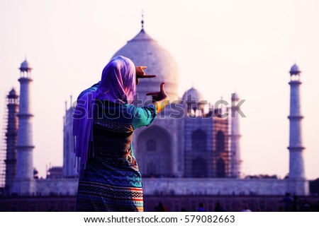 Young christian woman in traditional indian clothes in front of Taj Mahal in Agra, India taking a picture on a phone. UNESCO World Heritage Site. Mosque. Mausoleum.
