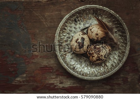 Three fresh raw quail eggs on vintage metal plate on a rustic wooden background. dark and moody toned picture. top view and space for text