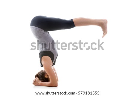 Young attractive woman practicing yoga, headstand exercise, variation of salamba sirsasana pose, working out, wearing black and grey sportswear, full length, isolated against white studio background