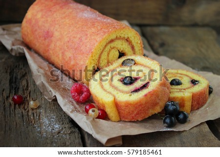 Swiss sponge roll biscuit cake with black currant and raspberry. On wooden background. Selective focus.