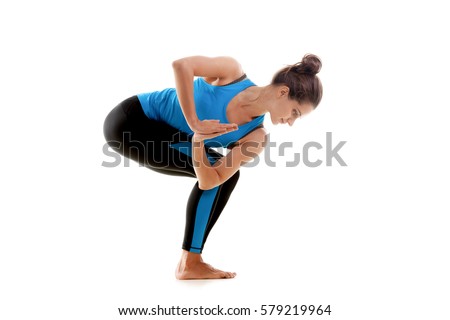 Young woman practicing yoga, standing in Parivrtta Utkatasana exercise, Revolved Chair pose, working out, wearing sportswear, blue tank top, pants, full length, isolated, white studio background