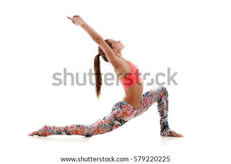 Young attractive woman practicing yoga, standing in anjaneyasana exercise, Horse rider pose, working out, wearing sportswear, red sport bra, pants, full length, isolated, white studio background Royalty-Free Stock Photo #579220225