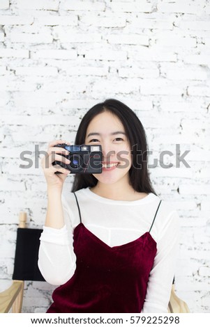 Asian woman pointing a retro camera in front in vintage wall