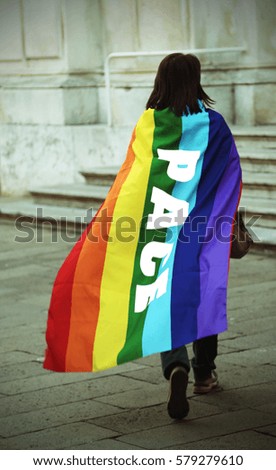 woman walking with multicolored flag with the inscription PACE which means peace in Italian on her back