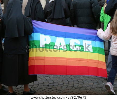 nun with a black veil and a little girl holding the colorful flag with the inscription PACE which means peace in Italian during a peace demonstration