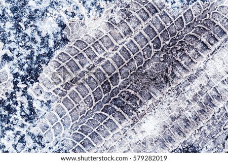 Diagonal traces of car tires in the snow on the asphalt. Close up view from above, image in the blue tones