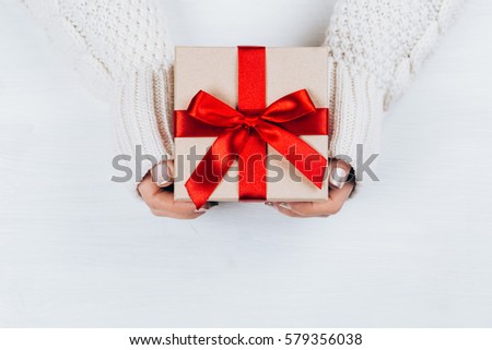 Female hands holding present with red bow on white rustic background. Festive backdrop for holidays: Birthday, Valentines day, Christmas, New Year. Flat lay style