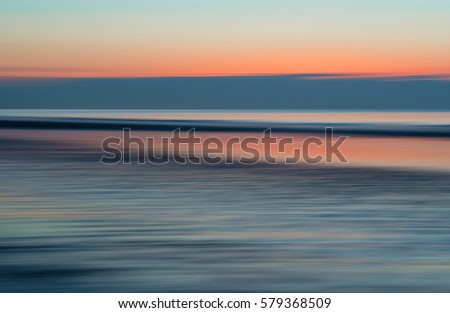 An abstract sunset with a long exposure along a beach with pink and orange colors to create movement.