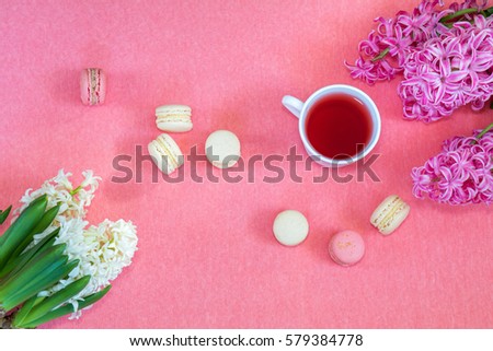 Beautiful spring holiday background. Cup of tea, fresh white and pink hyacinth and sweet  berry and vanilla macaroons cookies on pink copy space groundwork