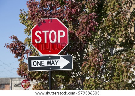 Stop sign and one way sign against a tree in the autumn